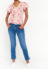 Květinový top v růžové a krémové barvě s výstřihem do V a zlatým lemováním. V kombinaci s modrými upnutými džíny a bílými teniskami.