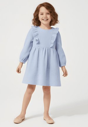 Jasnoniebieska sukienka z teksturowanej tkaniny, ozdobiona falbanami wzdłuż dekoltu i balonowymi rękawami, zestawiona z beżowymi balerinami.