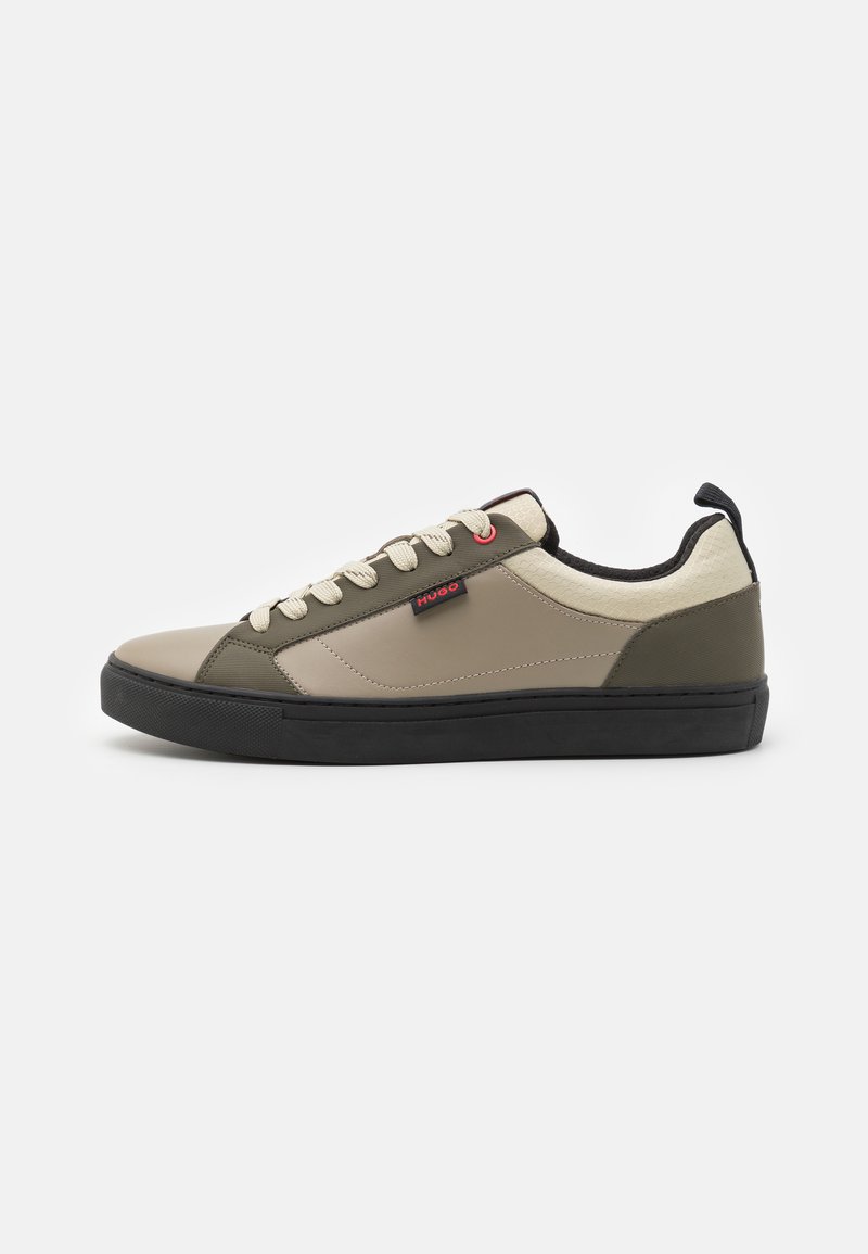 Lace-up sneaker featuring a blend of beige and olive green materials, black rubber sole, textured panel accents, and a small logo detail.