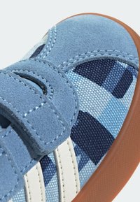 Blå mockaskor med ett spänne av kardborre, rutigt textilmönster i olika blå nyanser och en brun gummisula.