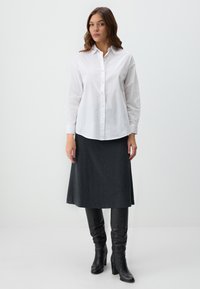 Witte knoop-overhemd, lange mouwen, katoenen materiaal. Donkergrijze rok tot de knie, gestructureerde stof. Zwarte hoge haklaarzen tot de knie.