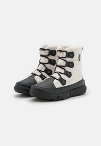 Botas de imitación de piel de color negro y crema forradas con pelo, con seis cierres de toggle, que cuentan con una suela negra texturizada, diseñadas para confort y calidez.