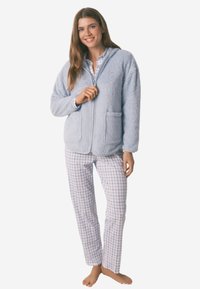 Blaue Fleece-Jacke mit Reißverschluss und Fronttaschen, kombiniert mit hellen, karierten Schlafanzügen. Weicher Stoff und entspannter Schnitt für hohen Tragekomfort.