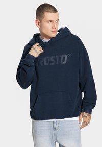 Granatowa bluza z kapturem z du żym, tonalnym logo "PROSTO" z przodu, z przednią kieszenią i ściągaczami przy mankietach. Miękka w dotyku.