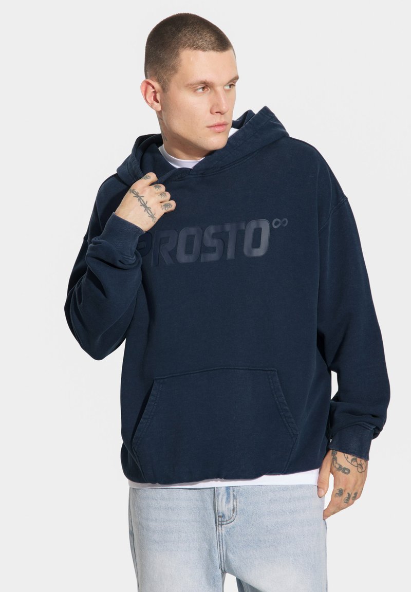 Granatowa bluza z kapturem z dużym, tonalnym logo "PROSTO" z przodu, z przednią kieszenią i ściągaczami przy mankietach. Miękka w dotyku.