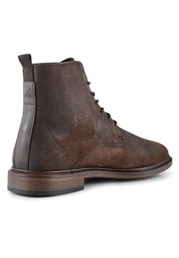 Botas de tobillo de ante marrón con un acento de cuero liso, puntera redonda, cordones y un tacón de madera. Presenta una lengüeta en la parte posterior para facilitar su uso.