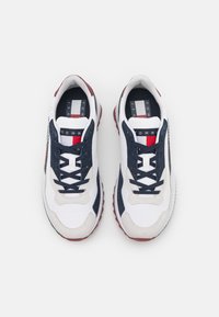 Scarpe da ginnastica bianche e navy con pannelli testurizzati, accenti rossi a contrasto e suola imbottita. Presentano lacci neri e dettagli con logo.