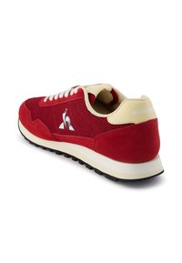 Sneaker rossa con tomaia in suede e mesh, lacci color crema e suola in gomma. Presenta un dettagli del logo sul lato e sul tallone posteriore. Design traspirante.