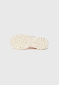 Sneaker-Sohle aus hellbraunem Gummi, mit einem strukturierten Muster für Grip, definierten Rillen und erhöhten Akzenten für Traktion.