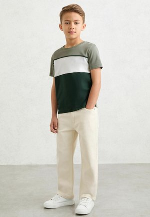 Szary i zielony T-shirt z krótkim rękawem i białym paskiem, zestawiony z beżowymi szerokimi spodniami i białymi tenisówkami. Prosty, codzienny strój.