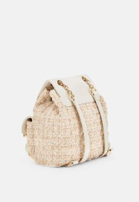 Beżowy plecak z fakturą, z kremowymi akcentami, złotym okuciem i podwójnymi szelkami; posiada zamek na sznurki oraz miękki, pleciony materiał.