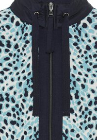 Fleece-Jacke mit blauem Leopardenmuster, marineblauem Kragen, Frontreißverschluss und Kordelzügen. Strukturierten Stoff mit kontrastierenden Musterdetails.
