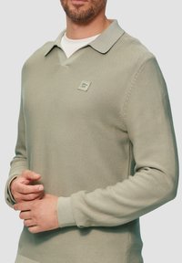 Hellgrünes Langarm-Poloshirt mit strukturierter Oberfläche, kragenförmigem Halsausschnitt und einem gewebten Markenpatch auf der Brust.
