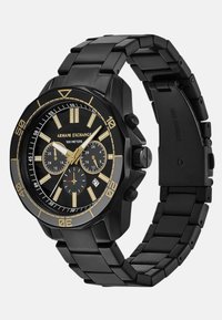 Črno nerjavnega jekla ura z izrazitim osemkotnim ohišjem, zlatimi poudarki, črnim številčnicami, kronografskimi podštevilčnicami in prikazom datuma. Vodoodporna do 100 metrov.