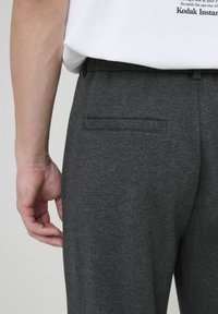Pantalons taillés gris foncé en tissu doux, dotés d'une poche arrière simple et d'une texture lisse, associés à un t-shirt blanc.