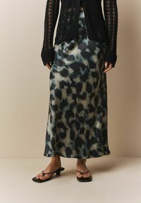 Maksi suknja od satena s leopard uzorkom u nijansama crne, tirkizne i bež boje, s lepršavim dizajnom i delikatnom teksturom. Uparena s crnim sandalama na vezanje.