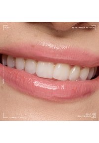 Lèvres brillantes rose clair souriant, montrant des dents blanches propres et une texture naturelle de la peau autour de la bouche, sans retouche de maquillage visible.