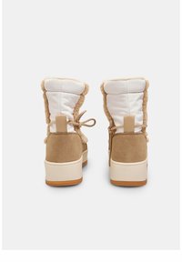 Botas de tobillo en color tostado y blanco con un suave borde de pelo sintético, acentos de ante y una suela de goma texturizada; cuenta con una lengüeta y un detalle de lazo.