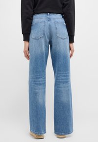 Ljusblå denimjeans med hög midja, vid benstil, två bakfickor och subtila slitningar på tygstrukturen.