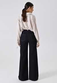 Crème blouse met puffmouwen en gestrikte manchetten, gecombineerd met hooghartige, donkere spijkerbroeken met flare en twee achterzakken.