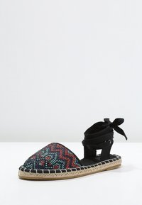 Sandal espadrilles intrecciate nere e multicolori con punta a punta, suola in corda e lacci per la caviglia regolabili. Presenta motivi geometrici.