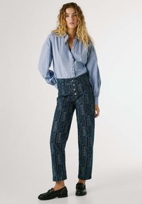 Blue, button-up shirt with long sleeves; high-waisted patterned trousers in dark blue, featuring decorative buttons and a floral design.
