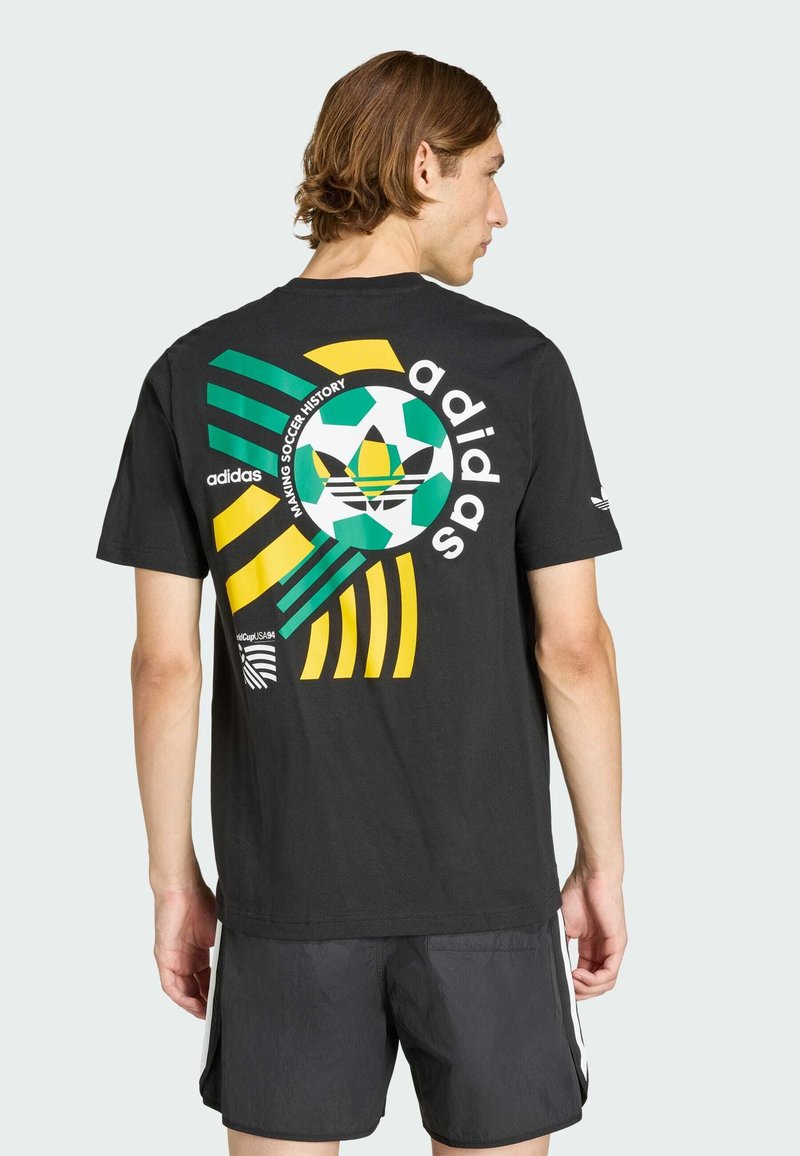 T-shirt en coton noir avec un graphique coloré de football au dos, avec des rayures vertes, jaunes et blanches, et une marque Adidas.
