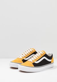 Yellow and black suede sneakers with white accents, featuring a rounded toe, flat white laces, and a rubber sole.