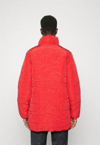 Rode gewatteerde jas met een hoge kraag, voorzien van een gestructureerd oppervlak en geperste patronen. Lange mouwen, relaxte pasvorm en middellange ontwerp.