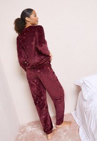 Burgundská sametová souprava na doma s hvězdnými vzory; volný top s dlouhými rukávy a kalhoty s elastickým pasem, texturovaný povrch.