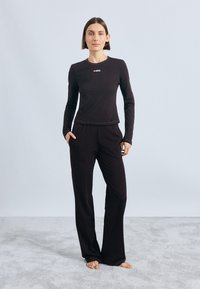 Camisola preta de mangas longas com decote redondo e um pequeno logotipo vermelho, combinada com calças pretas largas. Ambas feitas de um tecido suave.