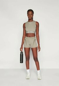 Szary sportowy crop top z opaską "NIKE PRO", pasujące szorty z wysokim stanem, czarna butelka na wodę i białe sneakersy na neutralnym tle.