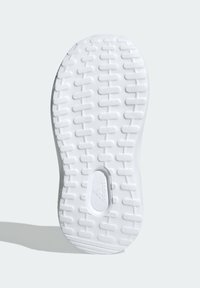 Biała gumowa podeszwa buta z teksturowanym prostokątnym wzorem bieżnika i wklęsłym logo Adidas na środku, na jasnym tle.