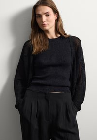 Suéter negro de punto con mangas texturizadas, combinado con pantalones negros holgados. La parte superior presenta un patrón acanalado y un corte relajado.