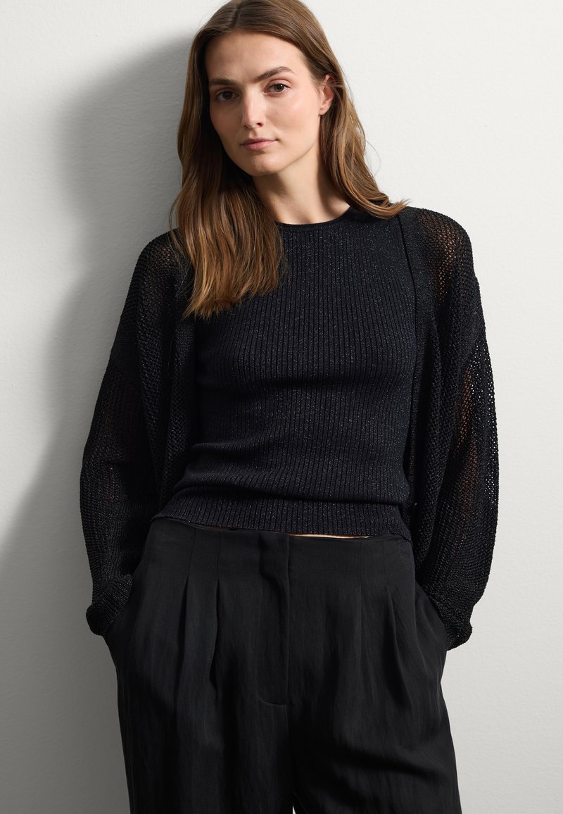 Suéter negro de punto con mangas texturizadas, combinado con pantalones negros holgados. La parte superior presenta un patrón acanalado y un corte relajado.