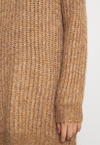 Maglione a maglia di un caldo colore marrone, caratterizzato da una texture a coste e maniche lunghe. Tessuto morbido con una vestibilità ampia e orlo con polsini.