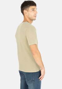 Helles beige Kurzarm-T-Shirt aus weicher Baumwolle mit Rundhalsausschnitt und lockerer Passform. Getragen mit blauen Jeans.