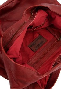 Sac à main en cuir rouge avec une texture douce, doté d'un intérieur en tissu assorti, d'une poche zippée et d'une étiquette en cuir de marque.