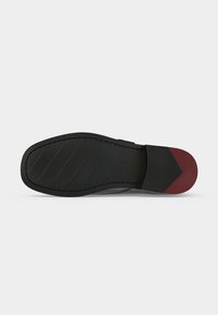 Semelle d'une chaussure de ville noire et rouge foncé avec un avant lisse et une zone de talon texturée sur fond gris clair.