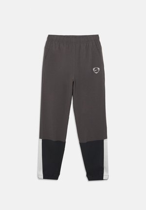 Dark gray and black athletic pants with elastic waistband, side pockets, and white stripe detail on lower legs and Nike logo on left thigh.