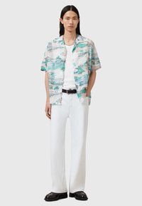 Camisa de manga corta con estampados de diseños tropicales en colores pastel, combinada con pantalones rectos blancos y zapatos negros.
