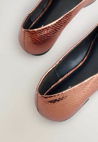 Ballerines en or rose avec un motif de peau de serpent texturé, bout rond et intérieur noir. La semelle extérieure est plate et fabriquée dans un matériau durable.