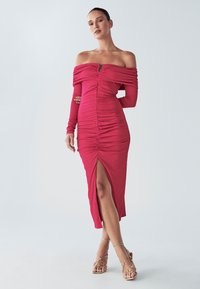 Šaty na ramená, priliehavé, v žiarivej ružovej farbe, s nariasenou textúrou, rozparkom vpredu a dlhými rukávmi, zvýrazňujúce siluetu.