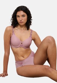 Lichtroze beha en bijpassende hoge tailleslip, voorzien van kantaccenten, gereedschaptextuur en een klein decoratief sieraad in het midden.