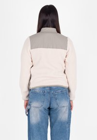 Fleecejack in crème met een lichtgrijze nylon schouderpartij, voorzien van een hoge kraag. Gepaard met vervaagde blauwe denim jeans met zichtbare zakken.