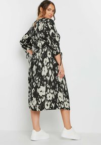 Svartvitt blommigt klänning med 3/4-långa ärmar, insvängd midja och nyckelhål i ryggen, bärs med vita sneakers. Slät tygtextur.