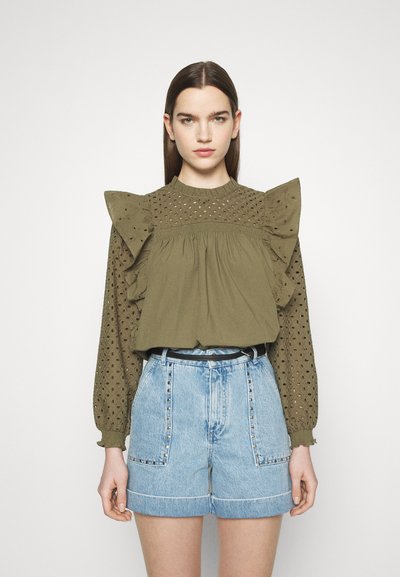 Blouse vert olive avec des détails en œillets et des manches volantes, assortie à un short en denim clair avec des poches embellies et une ceinture noire.