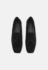 Sapatos slip-on em camurça preta com um design plano, apresentando franjas decorativas e um formato de ponta quadrada. Forro interior suave.