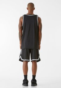 Melna sporta bez piedurknēm un šorti ar baltajiem akcentiem, ar brīvu piegriezumu, elpojošu materiālu un sporta iedvesmotu dizainu.