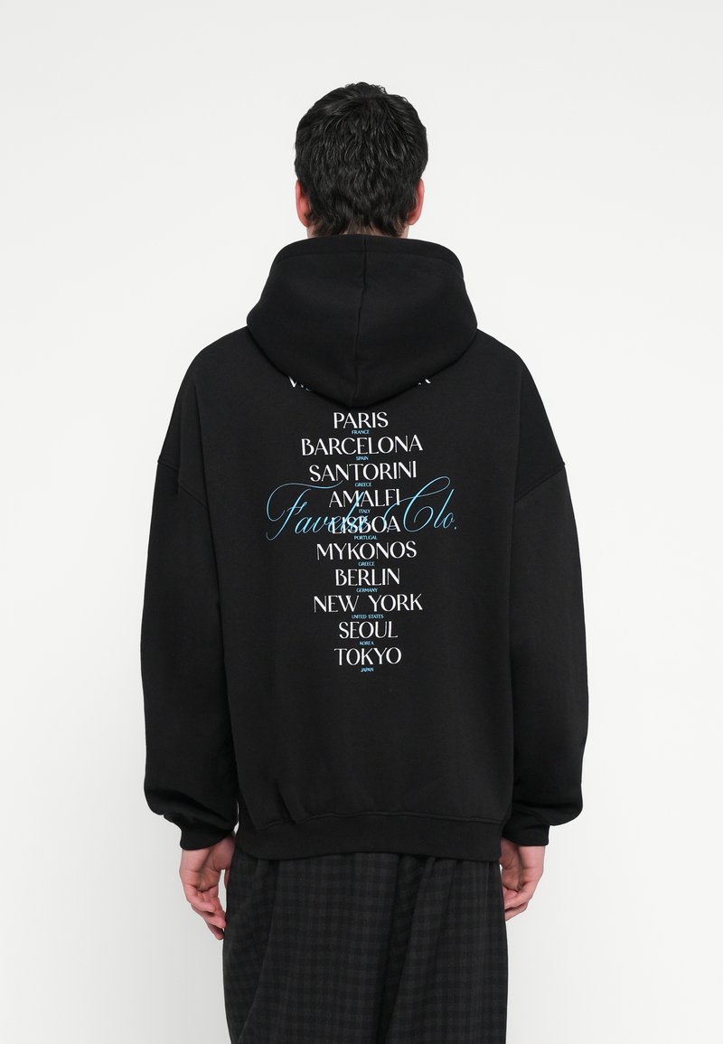 Hanorac negru, cu croială lejeră, având un imprimeu grafic cu nume de orașe în text alb și albastru pe spate. Material moale cu textură confortabilă.